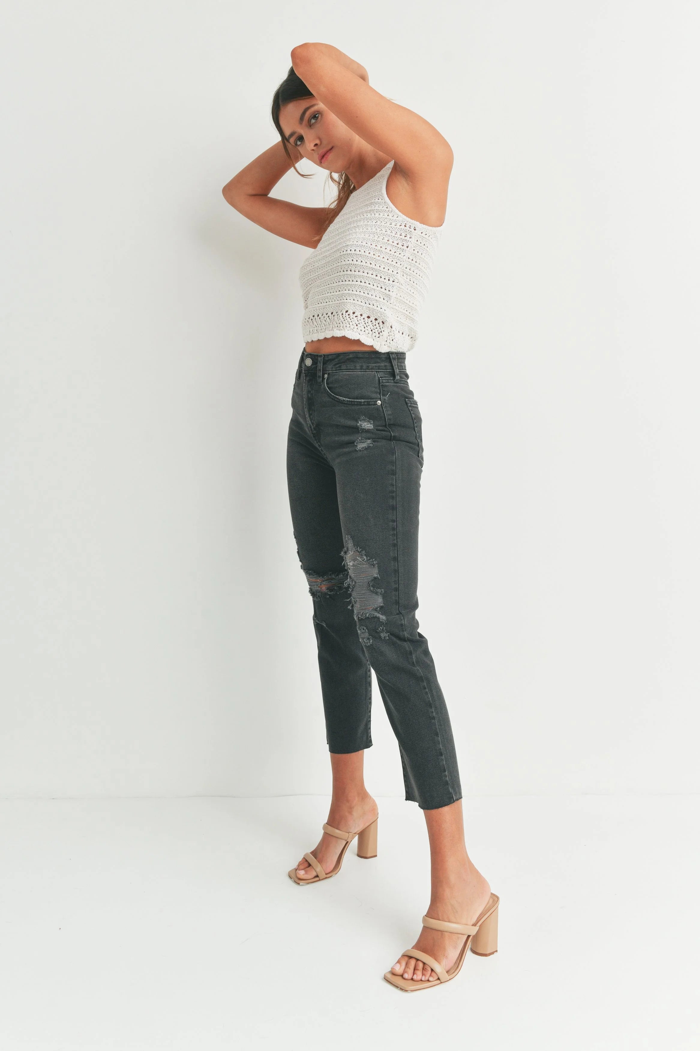 Woman wearing a white lace top and dark jeans on a white background
