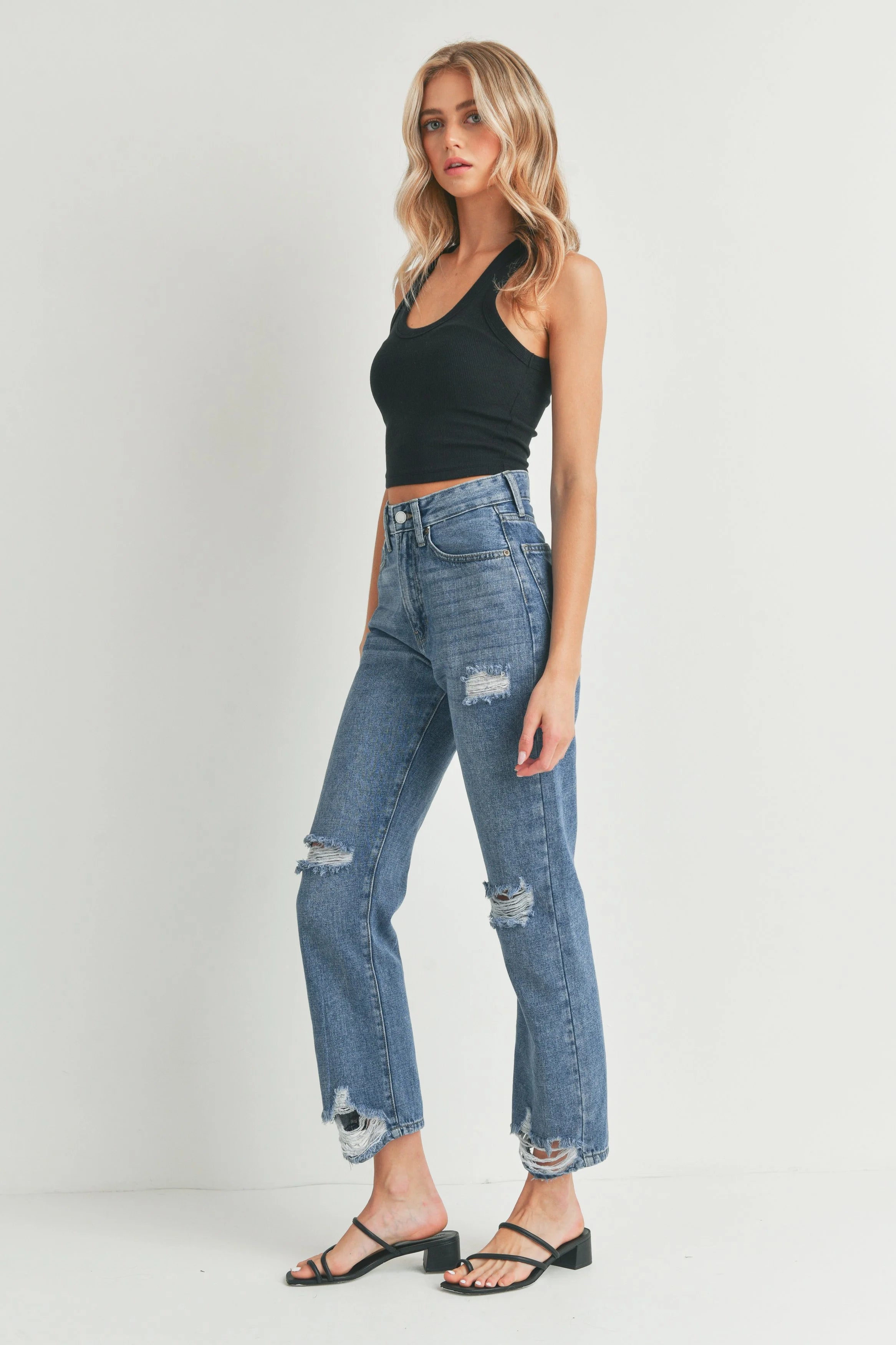 Woman wearing a black tank top and blue jeans on a white background