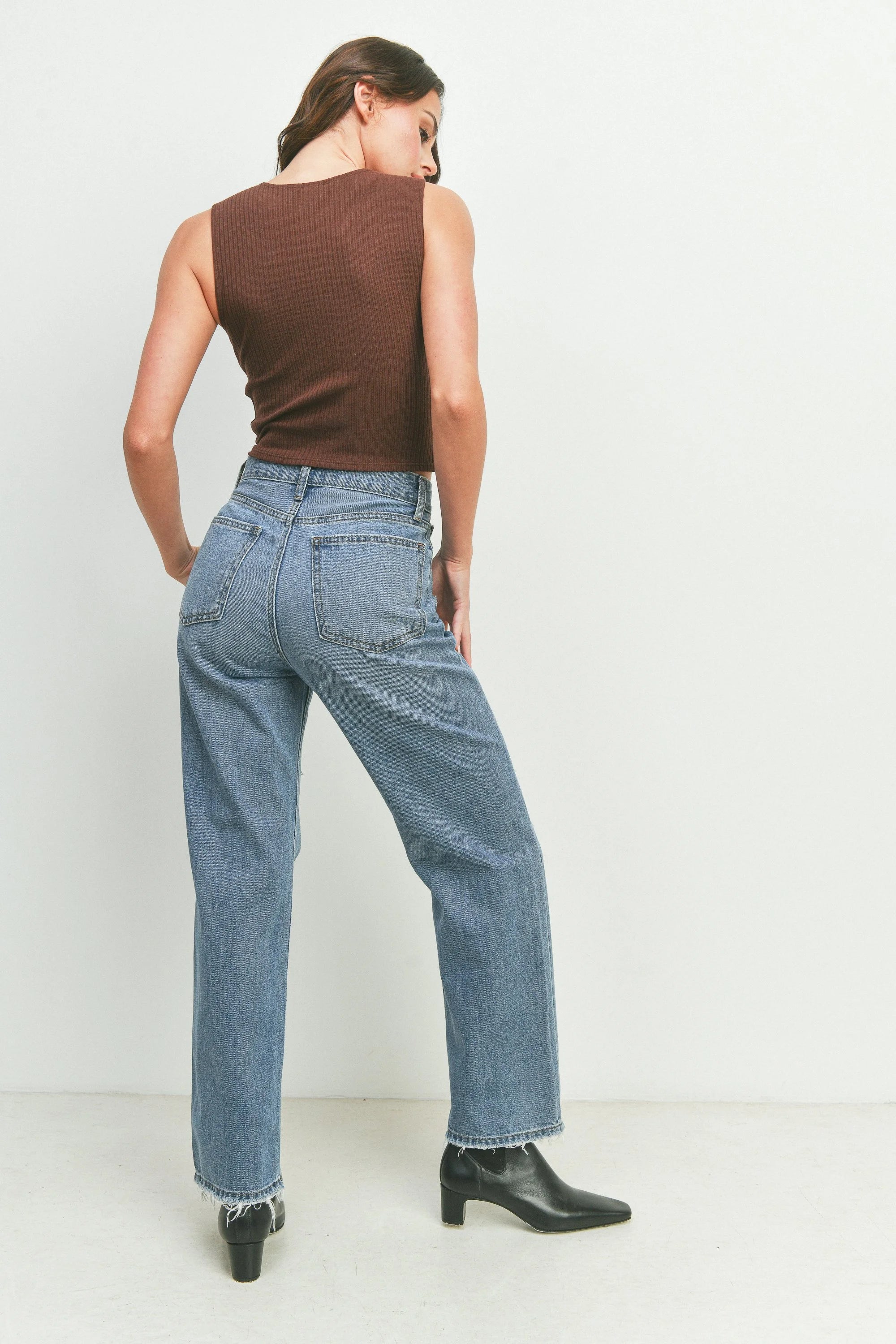 Person wearing a brown sleeveless top and blue jeans against a white background