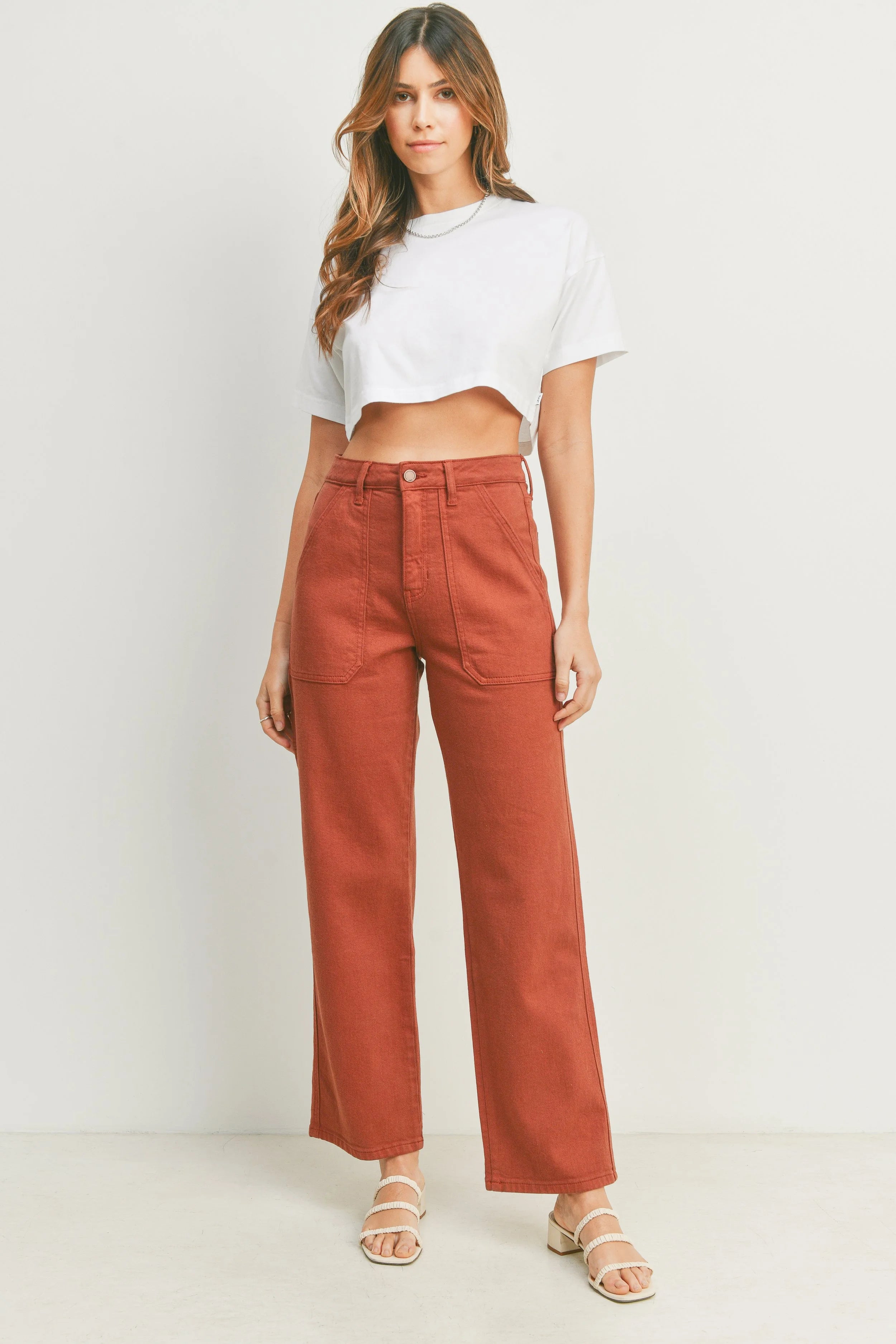 Woman wearing a white crop top and rust-colored pants on a white background