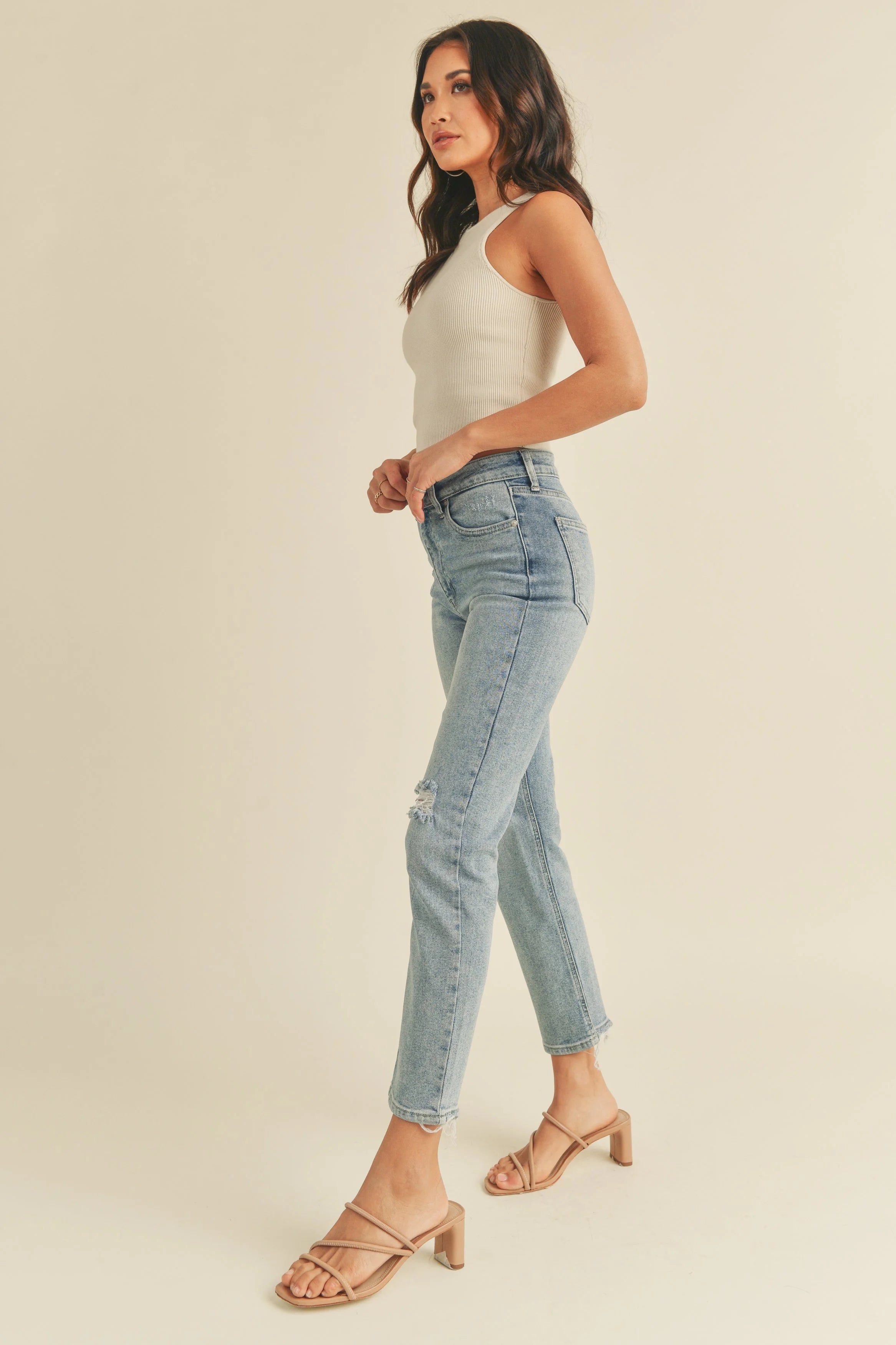 Woman wearing light blue jeans and a white top on a beige background