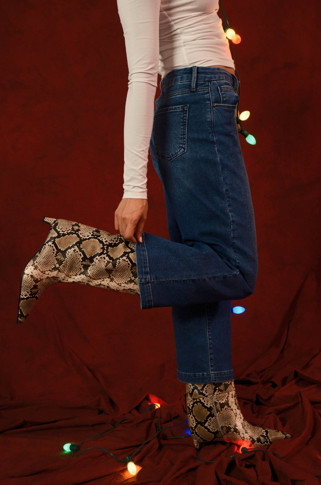 Person wearing snake print boots on a dark red background with string lights.
