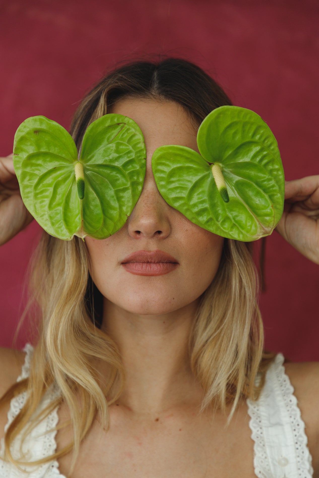 Woman holding green leaves over her eyes against a red background